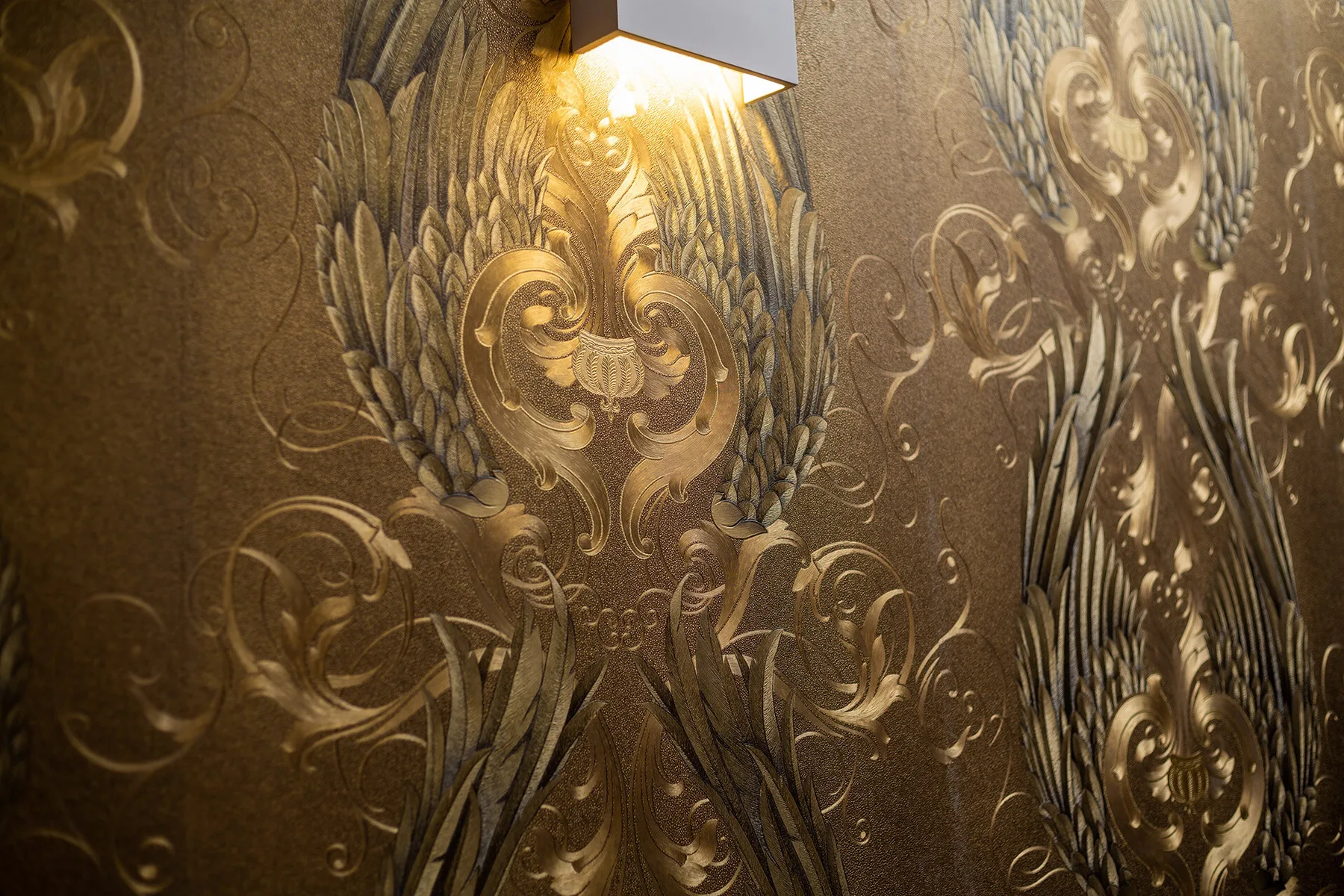 Espacio representativo del hotel: Pared con patrón ornamentado iluminada por una pequeña lámpara.