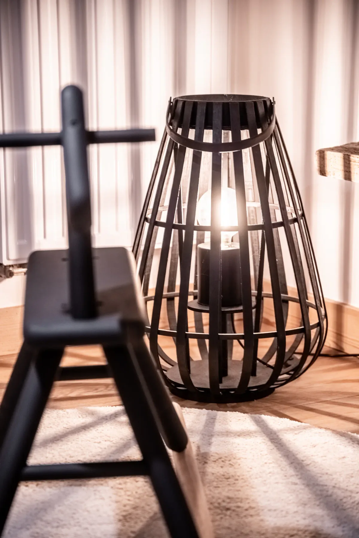 A warmly lit seating area features a sculptural black lantern beside a chair.