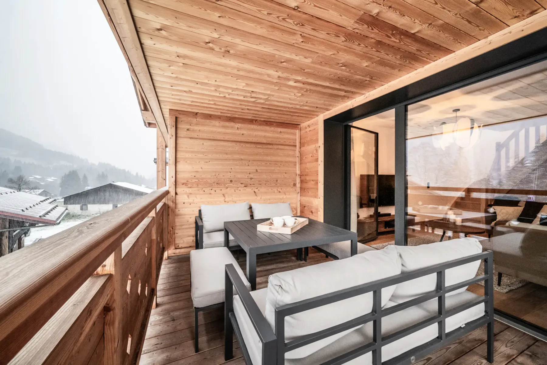 A covered wooden balcony with outdoor seating and large glass doors.
