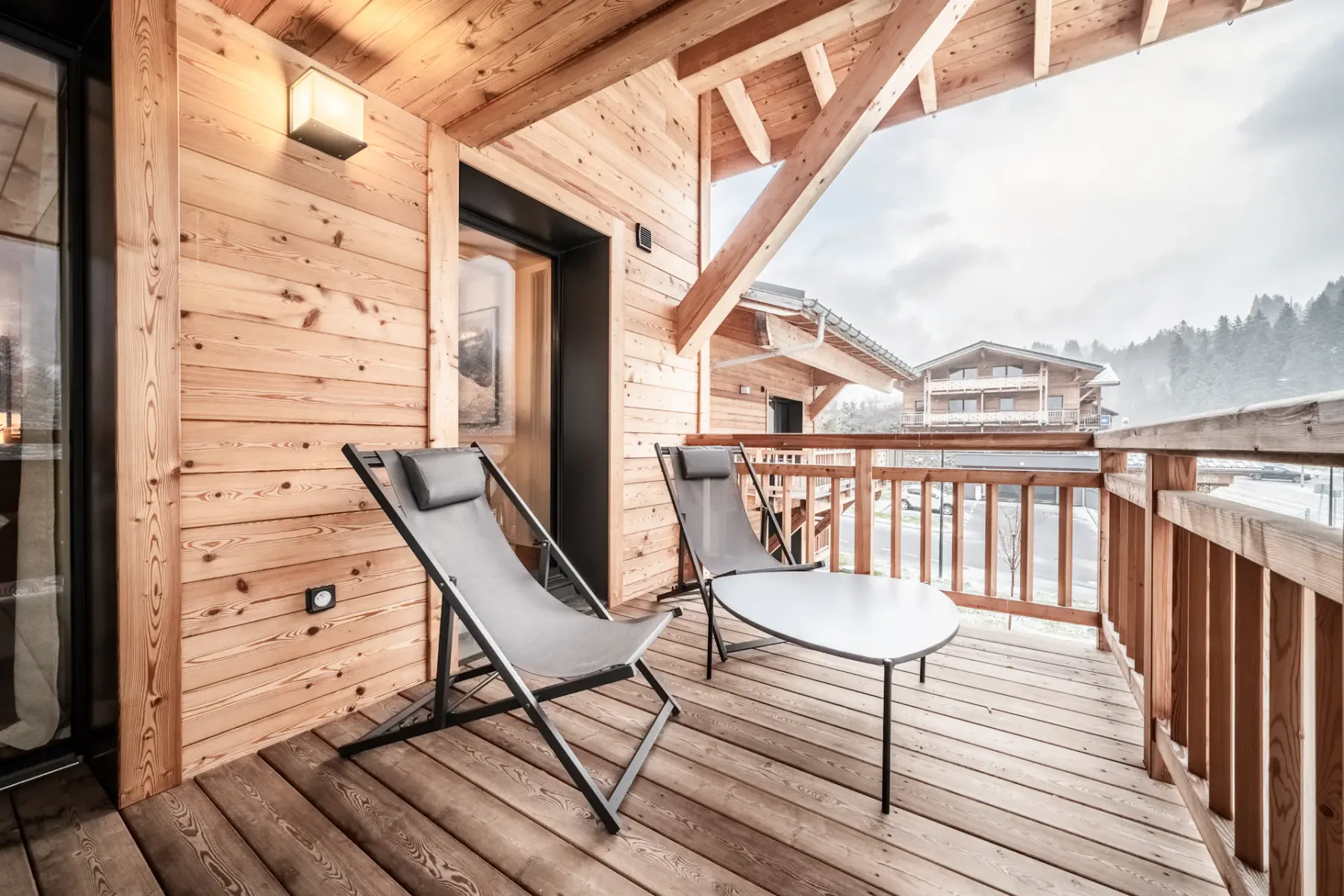 A covered wooden balcony has lounge seating and overlooks neighboring buildings.