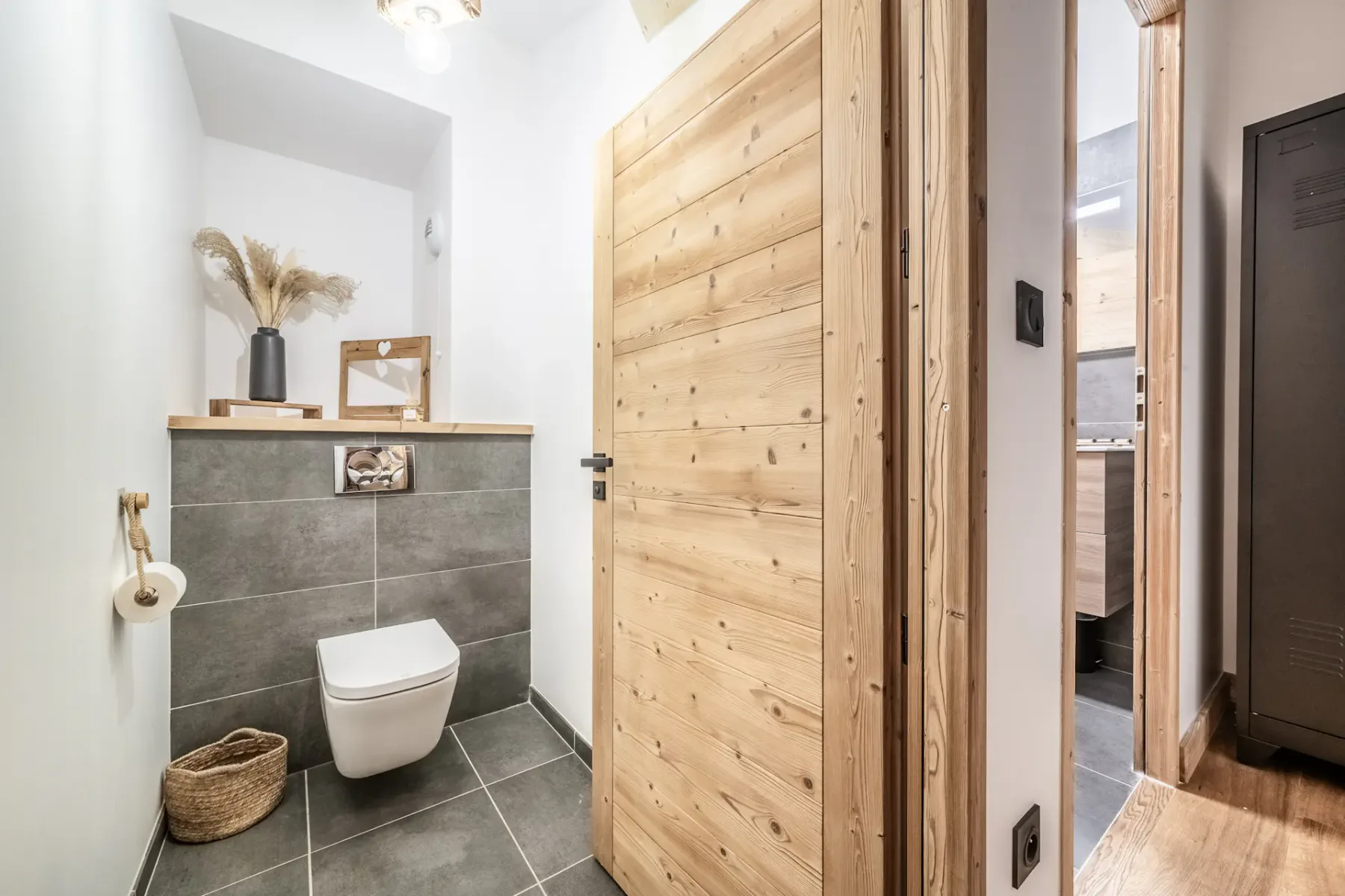 A tiled bathroom with a wall-mounted toilet and an open wooden door.