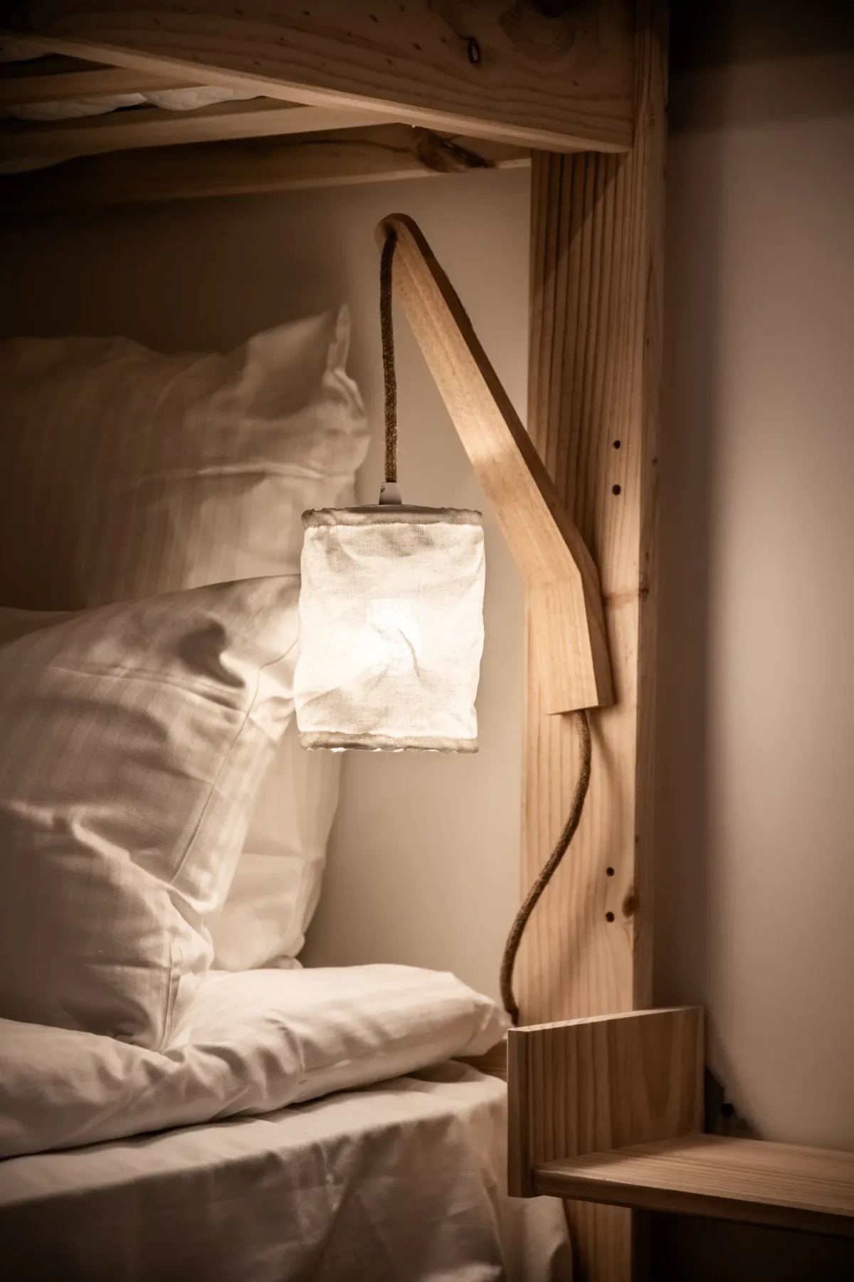 A bed with white bedding sits beside a small wall-mounted reading light.