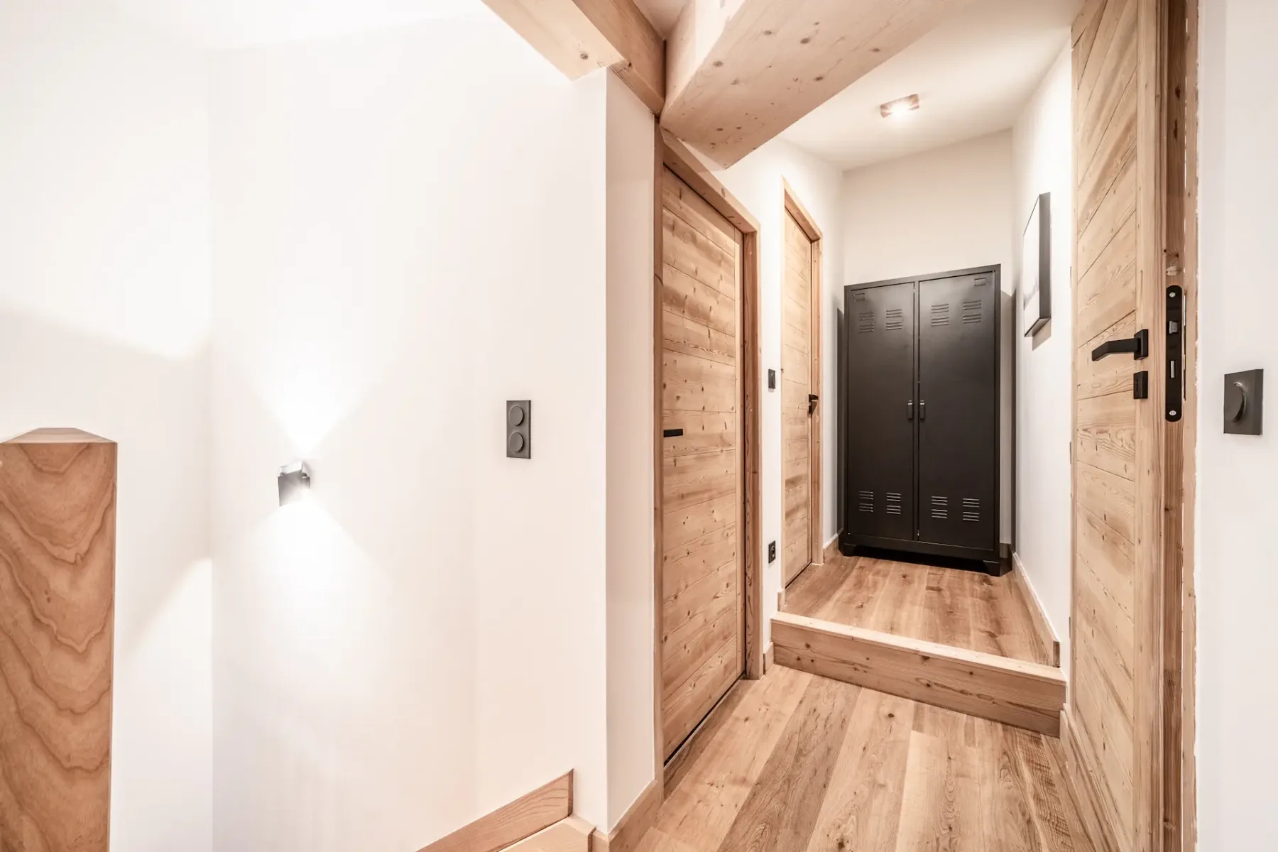 A bright hallway with wood-paneled doors and dark lockers at the far end.