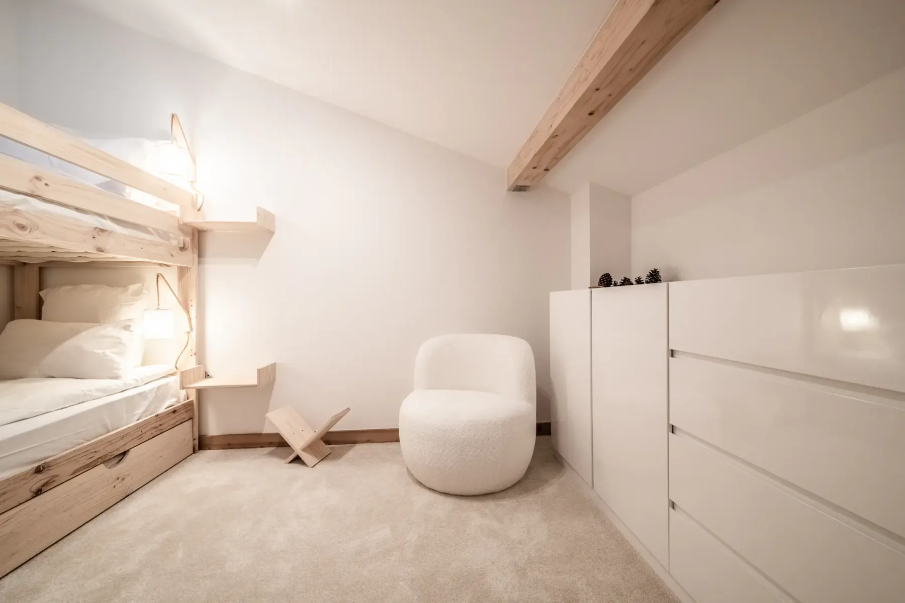 A bright bedroom with a built-in bunk bed, a white chair, and storage cabinets.