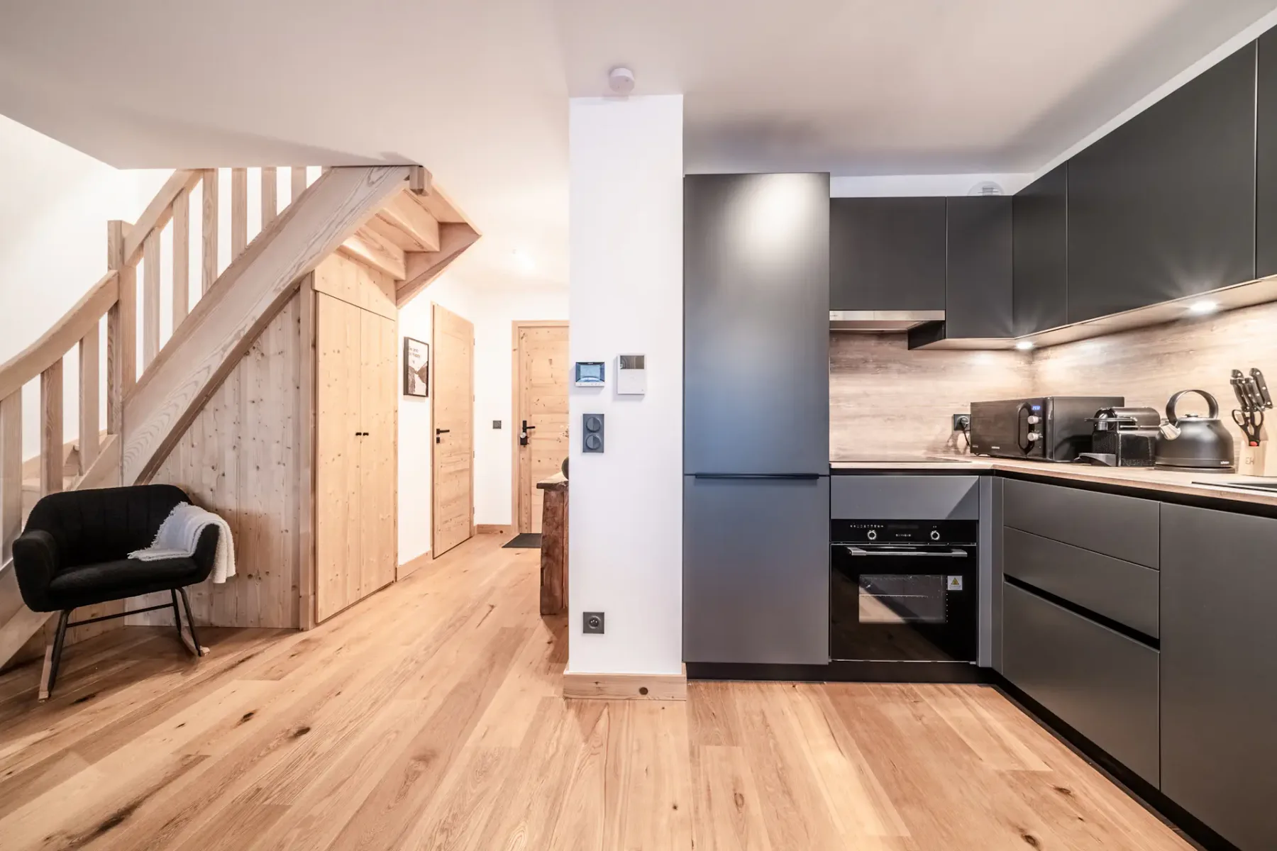 An open-plan kitchen and living area with dark cabinetry and a wooden staircase.