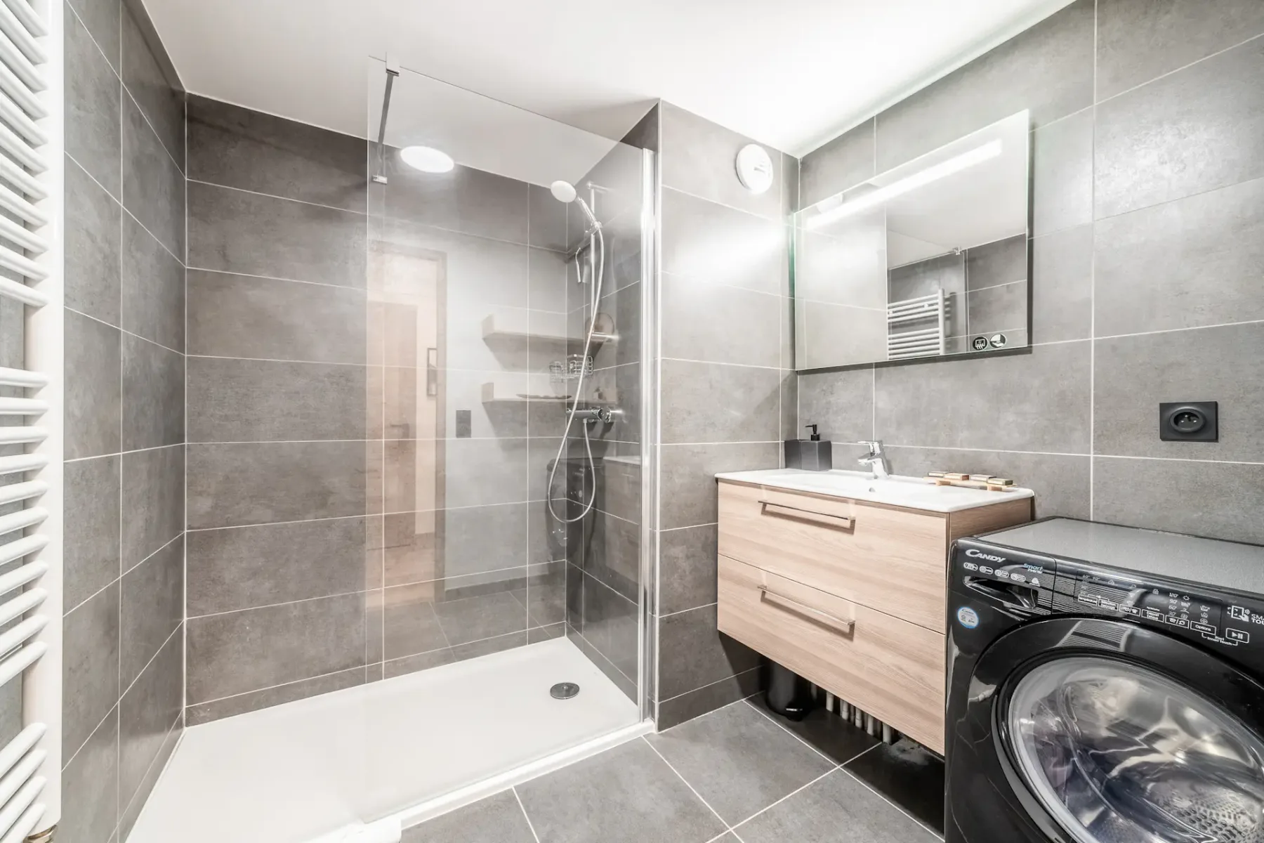 A modern bathroom with a glass shower, sink, and washing machine.