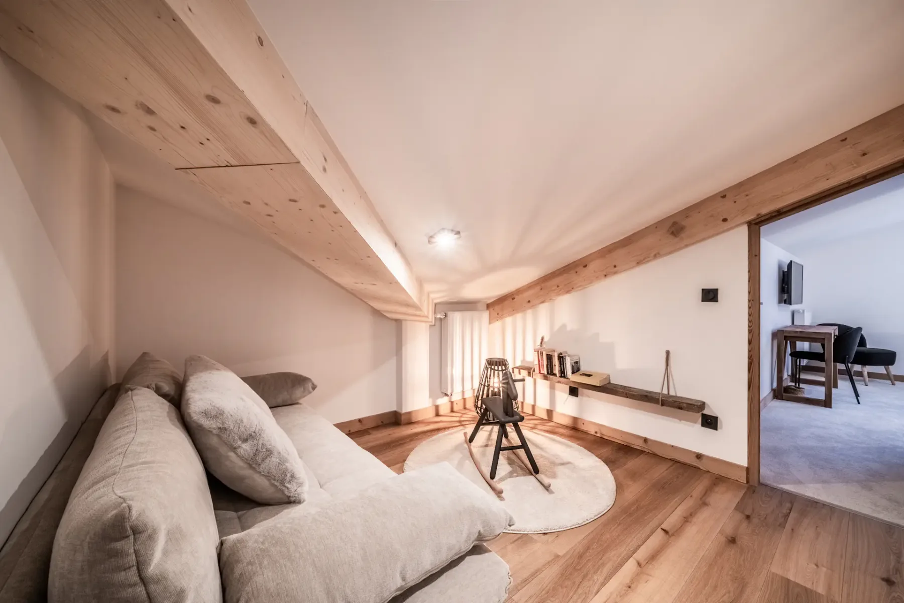 A cozy living area with floor seating and a low shelf beneath exposed wooden beams.