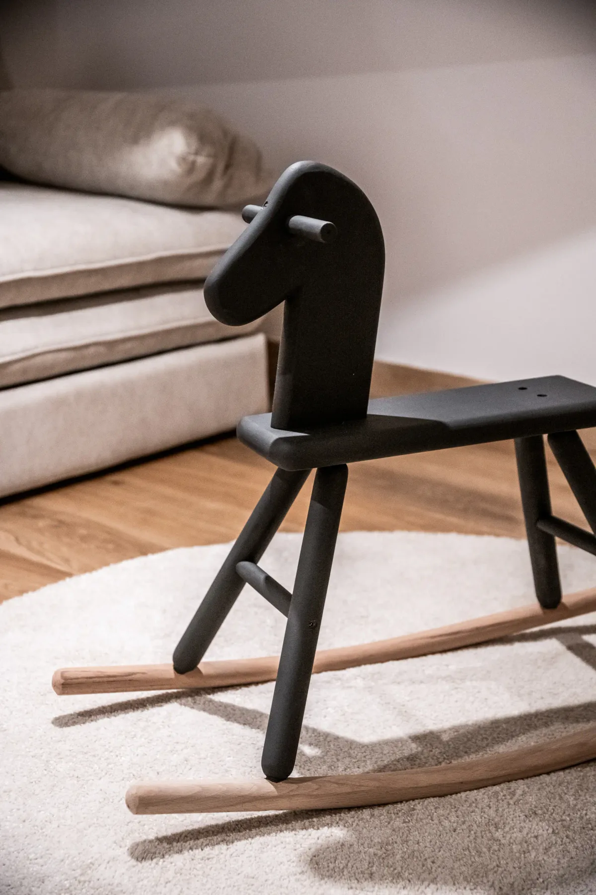 A minimalist rocking chair stands on a pale rug beside a beige sofa.