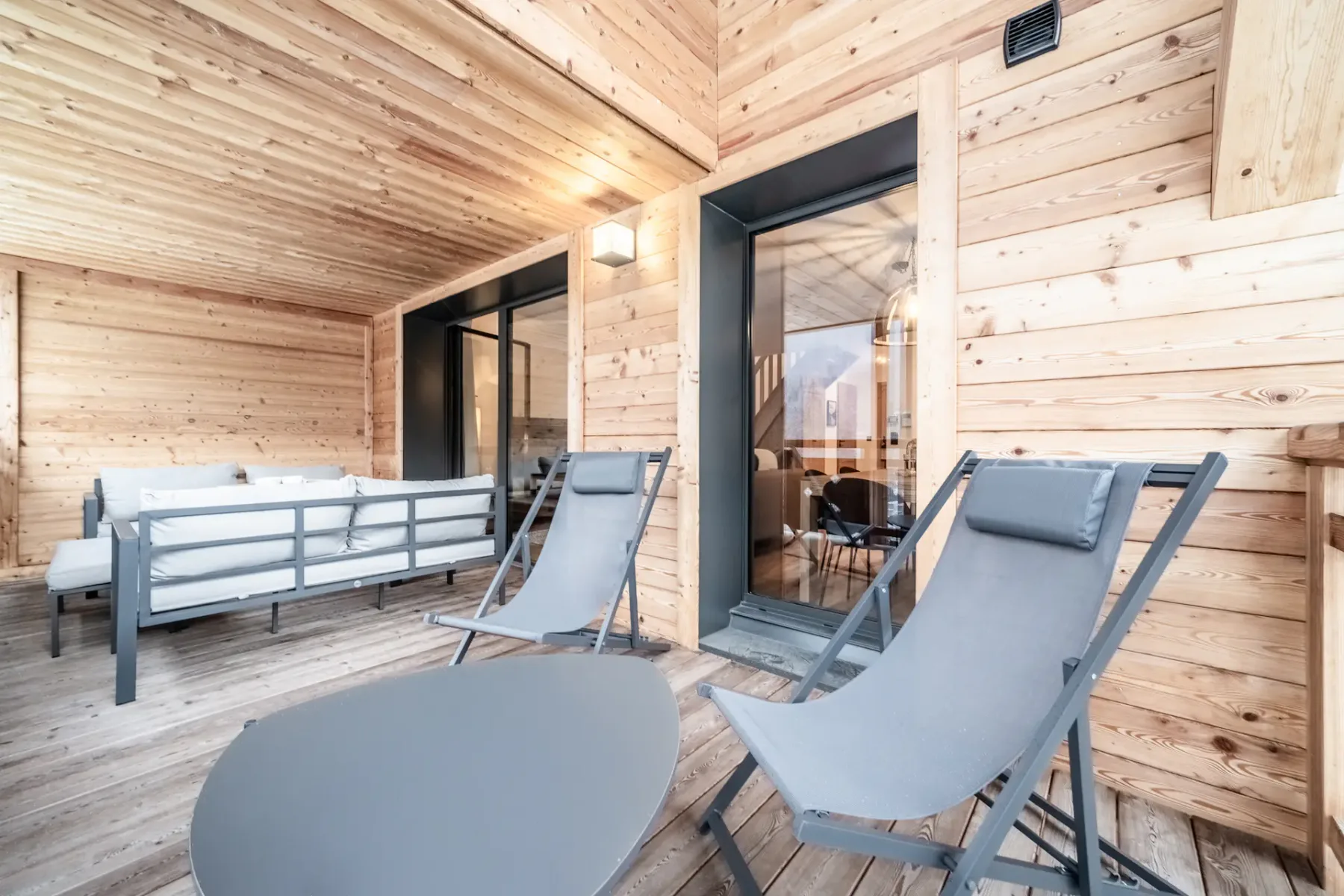 A wood-paneled patio with gray lounge seating and glass doors.