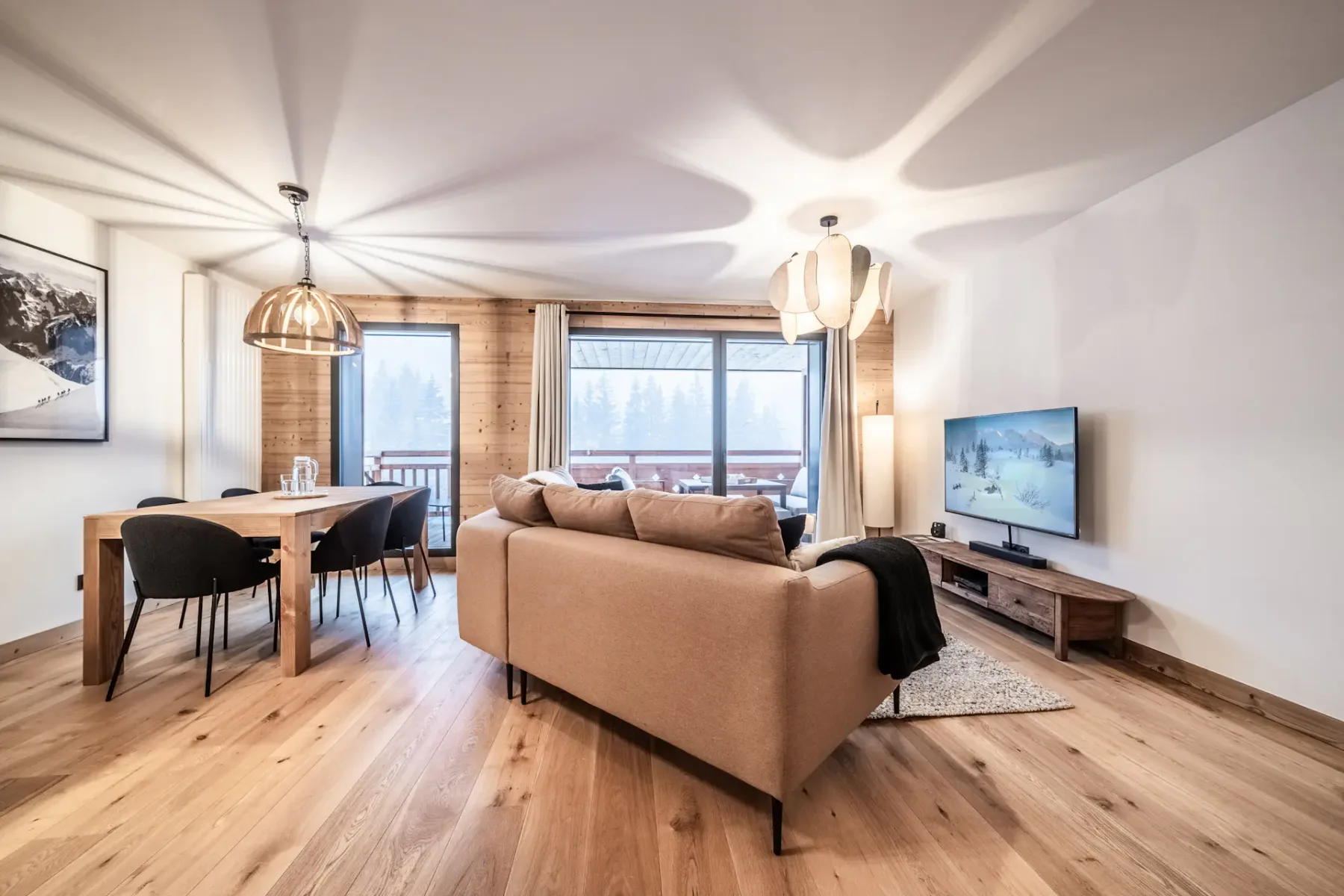 A bright living and dining area with seating, a dining table, and large windows.