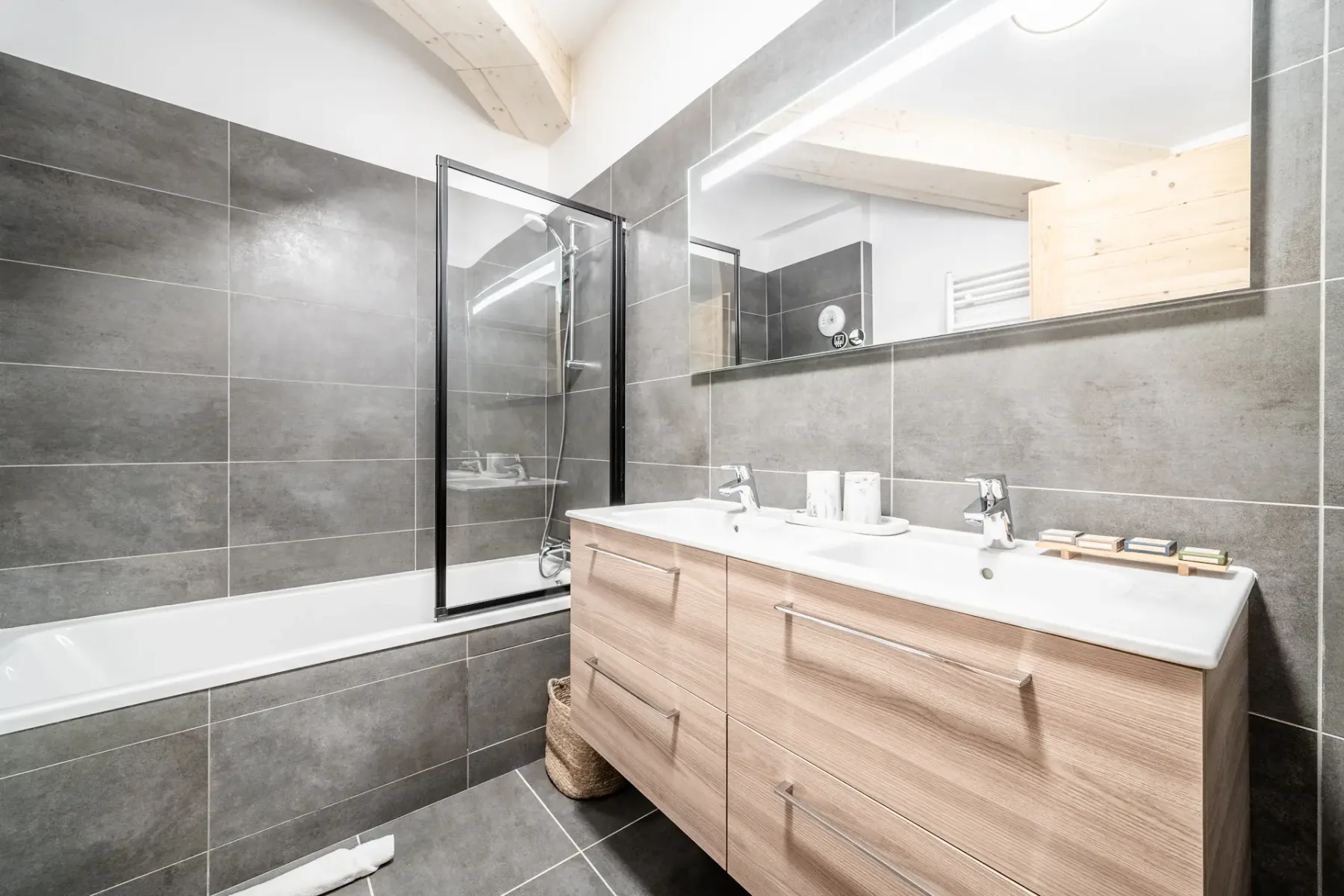 A tiled bathroom with a bathtub, glass shower screen, and wood vanity.