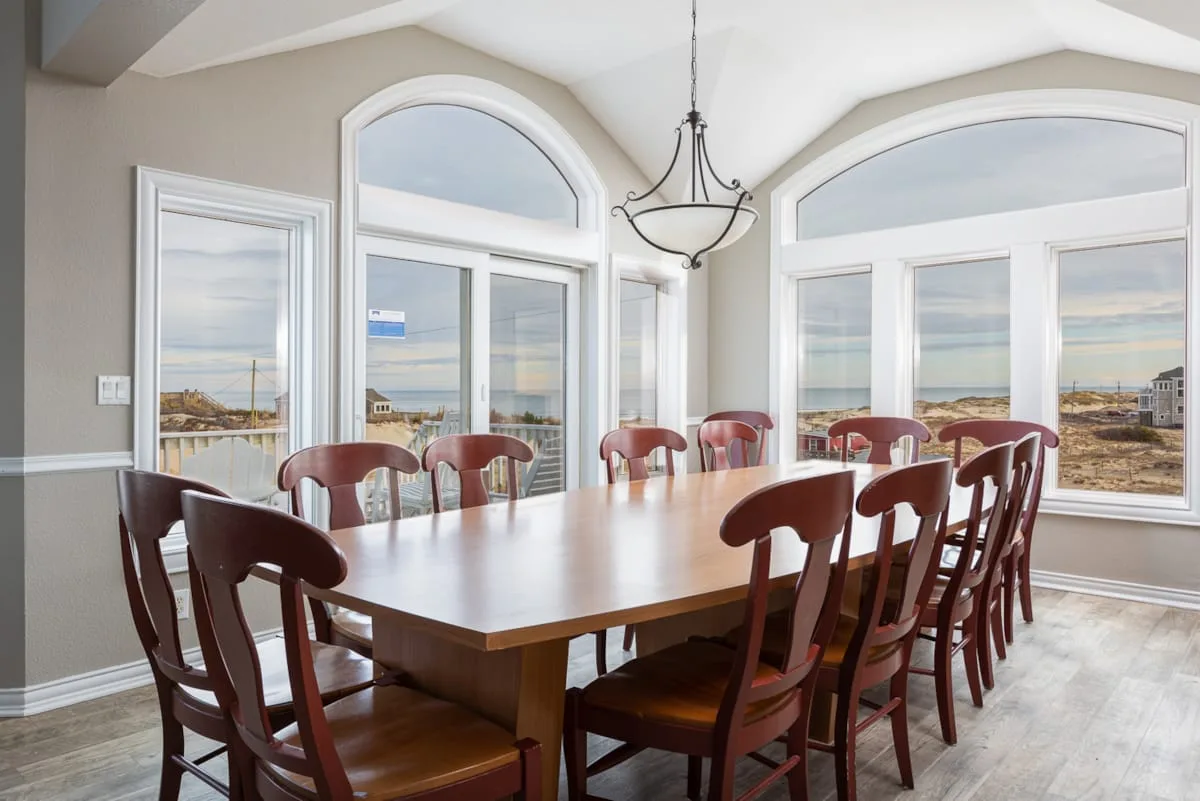 A dining room with a long table and large windows overlooking the water.