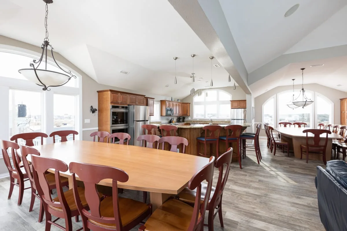 A spacious kitchen and dining area with wooden tables and large windows.