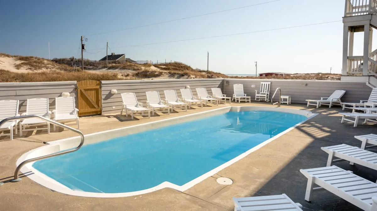 An outdoor swimming pool is surrounded by lounge seating on a sunny deck.