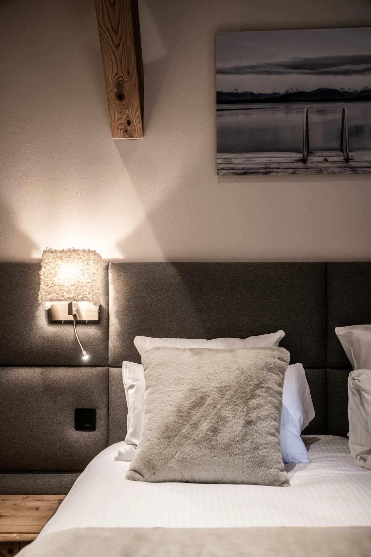A bedroom with a bed, upholstered headboard, and wall-mounted bedside light.
