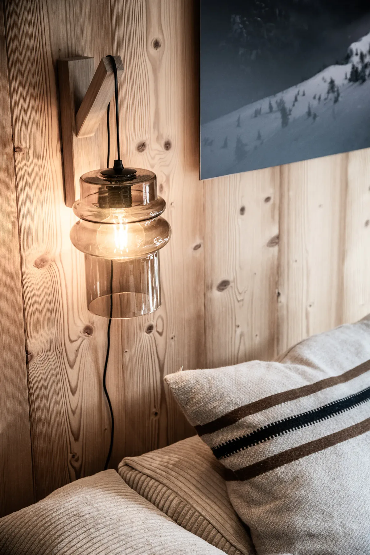 A bedroom corner with a glowing wall lamp and striped bedding.