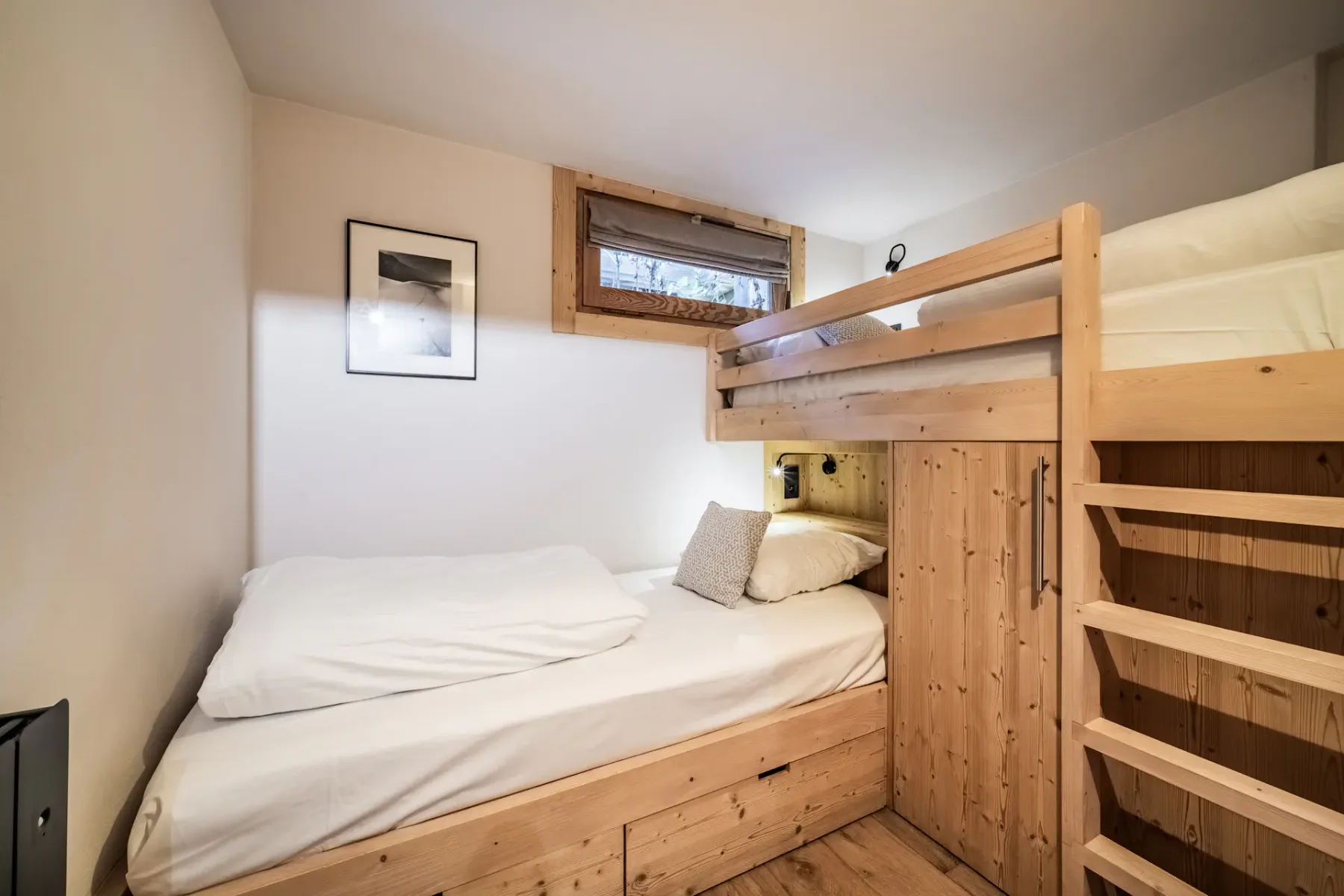 A compact bedroom with a lower bed beneath a wooden bunk bed.