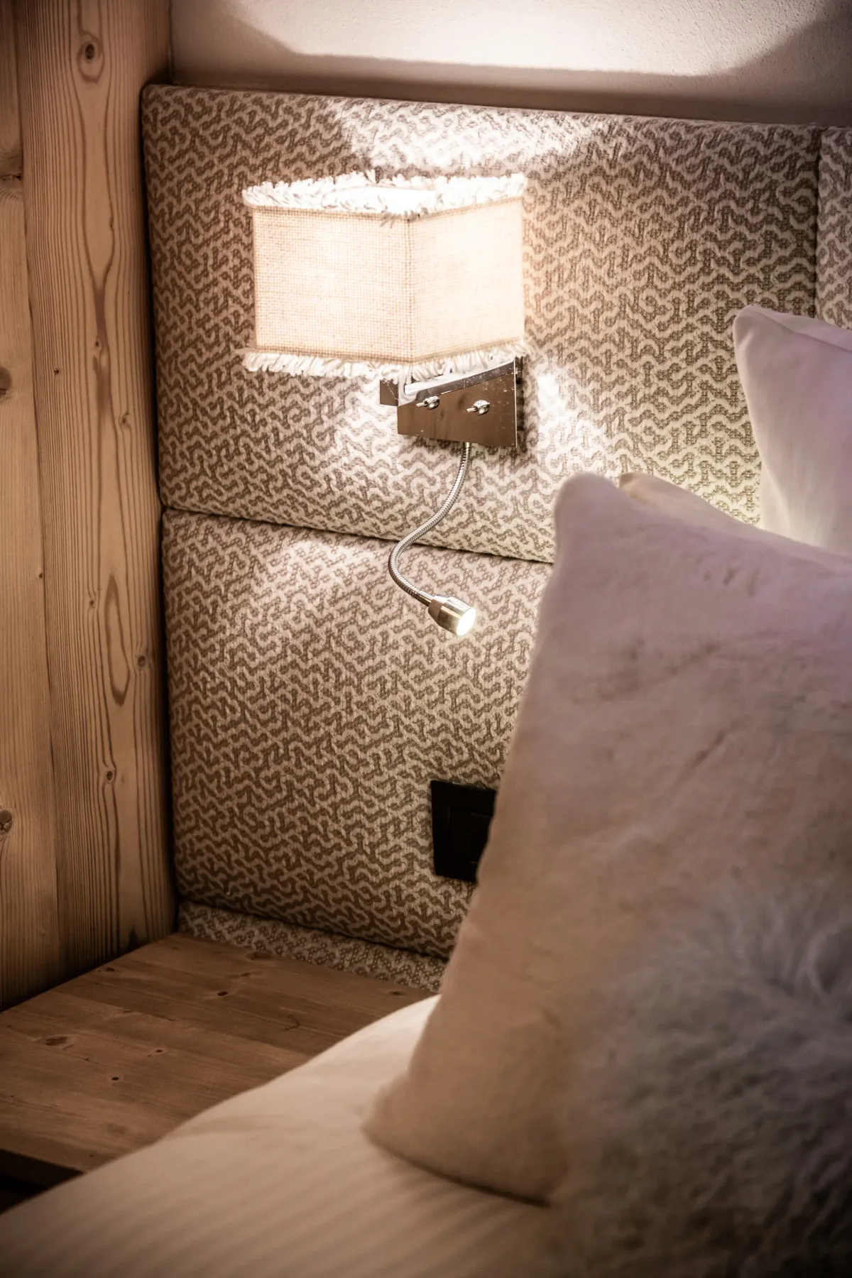 A bedroom corner with a lit wall lamp above the bed.