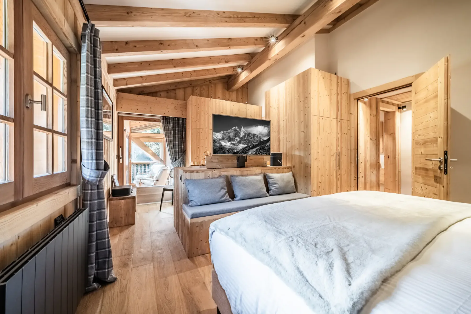A wood-paneled bedroom with a bed and a seating area beneath exposed beams.