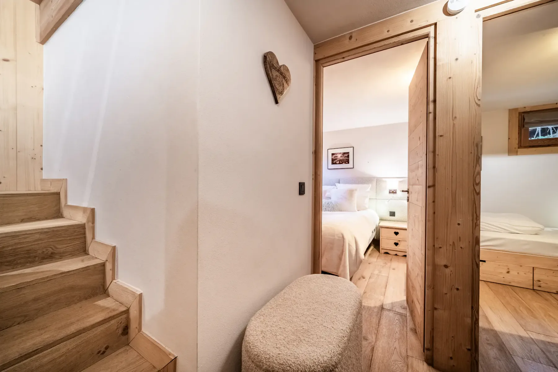 A wooden staircase and hallway lead to bedrooms with beds and bedside tables.