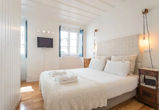 Un dormitorio luminoso con una cama bien arreglada y ventanas en la pared.