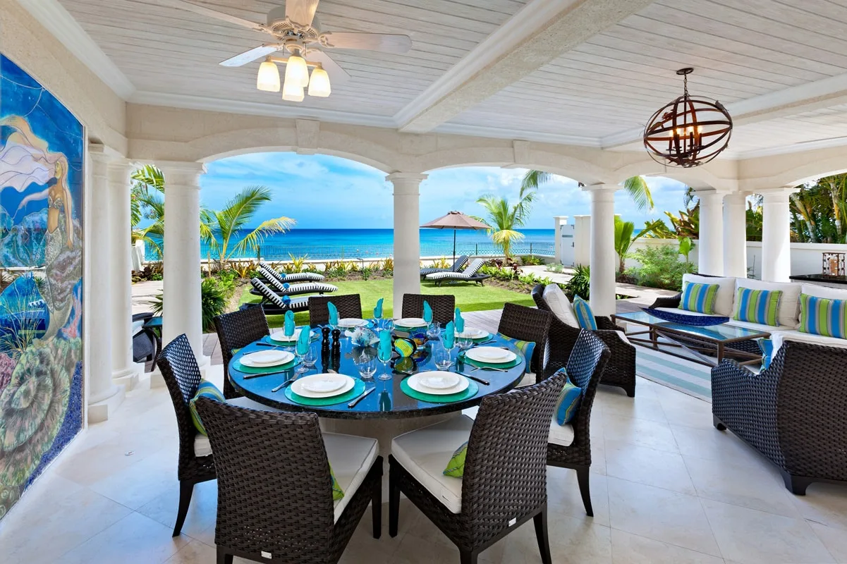 Covered outdoor dining area with a round table overlooking the ocean.