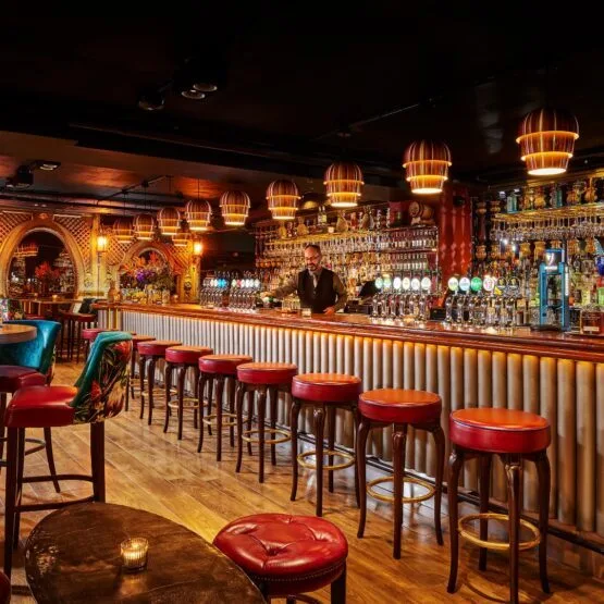 Representative hotel space: A warmly lit bar features a long counter lined with red stools.