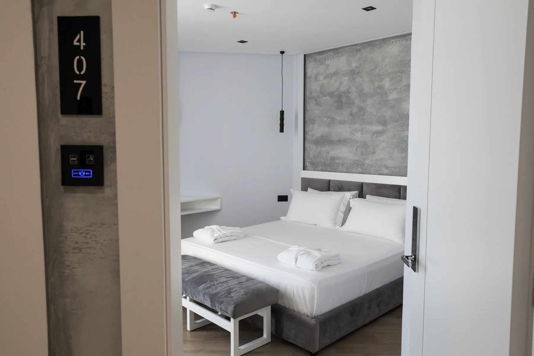 Espacio representativo del hotel: Un dormitorio moderno con una cama bien tendida y una pared decorativa gris.