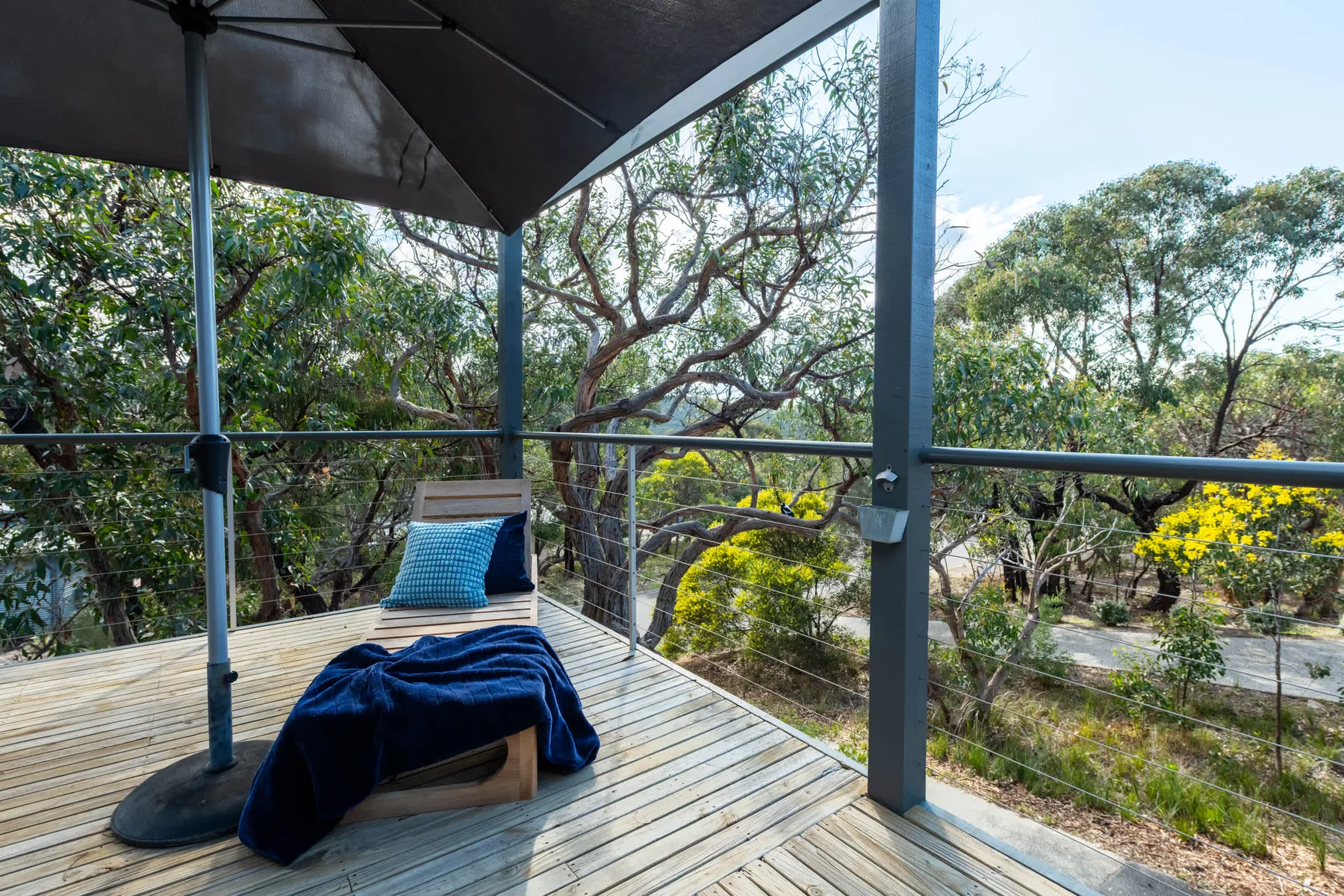 A covered outdoor deck with a lounge chair overlooking leafy trees.