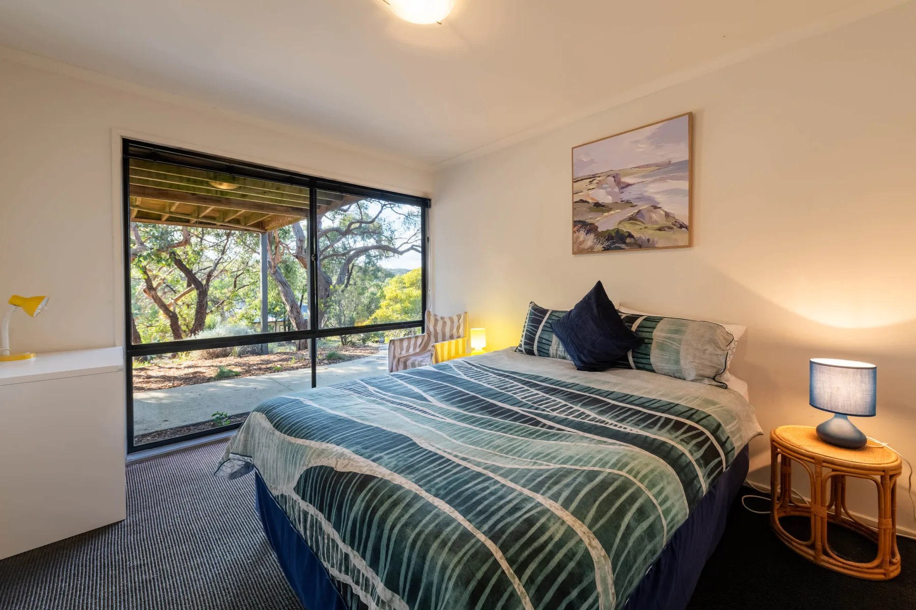 A bedroom with a bed beside a large window overlooking trees.