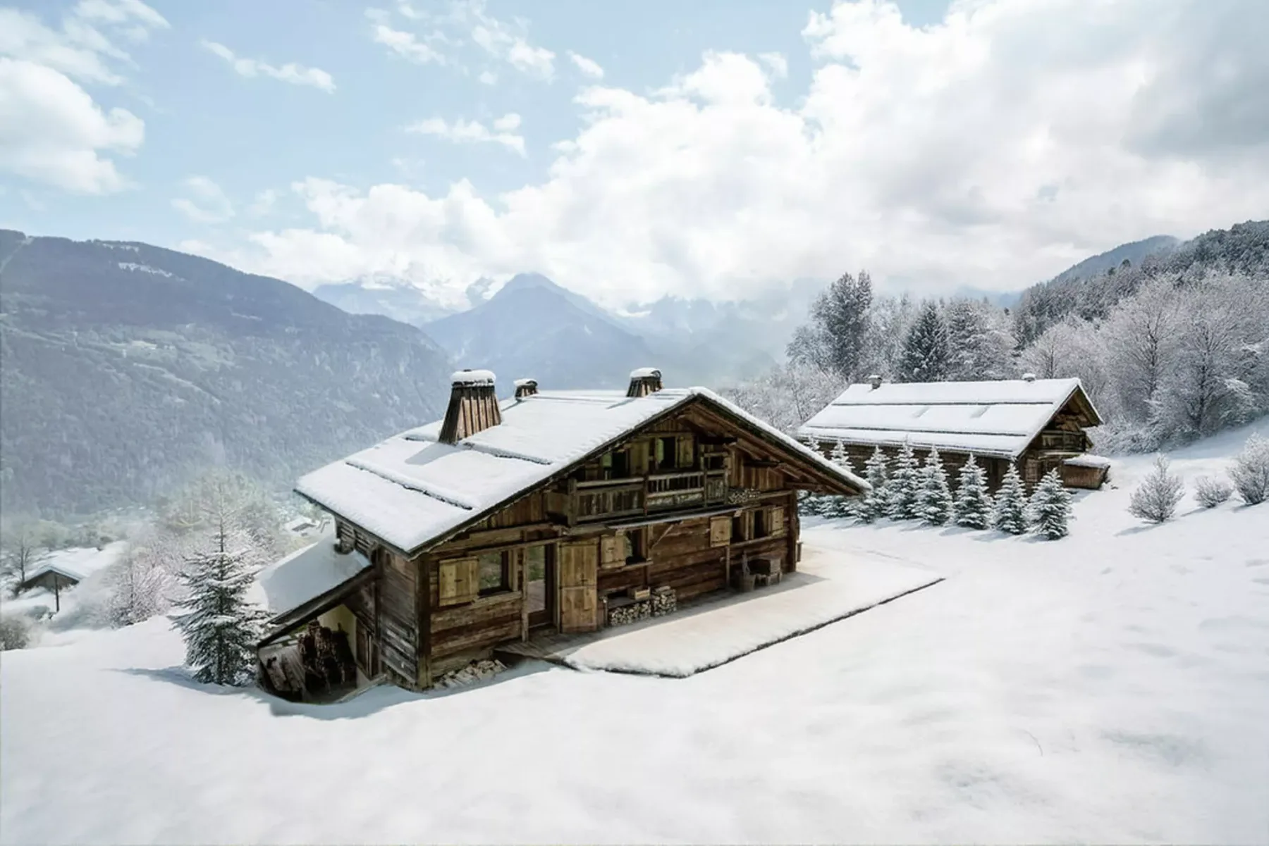 Snow-covered wooden cabins sit in a mountain landscape beneath a cloudy sky.
