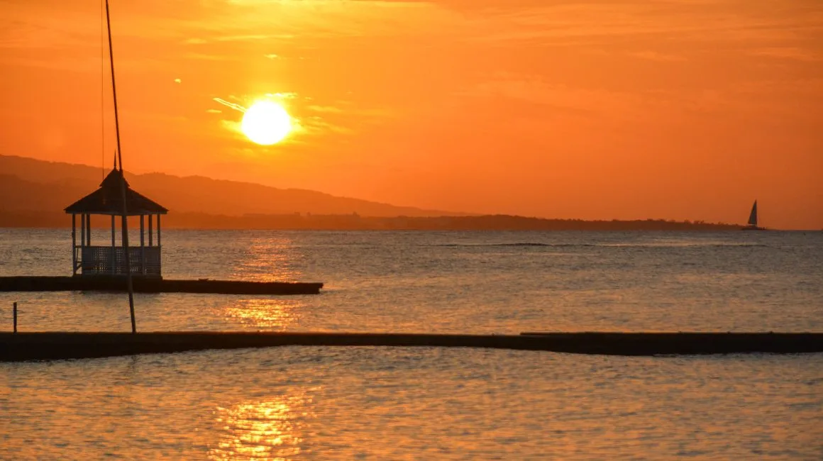 Espacio representativo del hotel: Atardecer sobre aguas tranquilas, con un pequeño pabellón silueteado cerca de la orilla.
