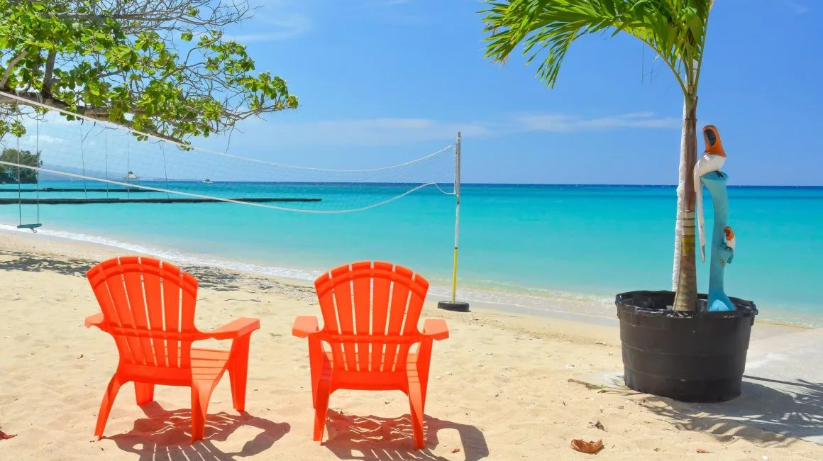 Espacio representativo del hotel: Una playa de arena con dos sillas de colores frente al agua turquesa.