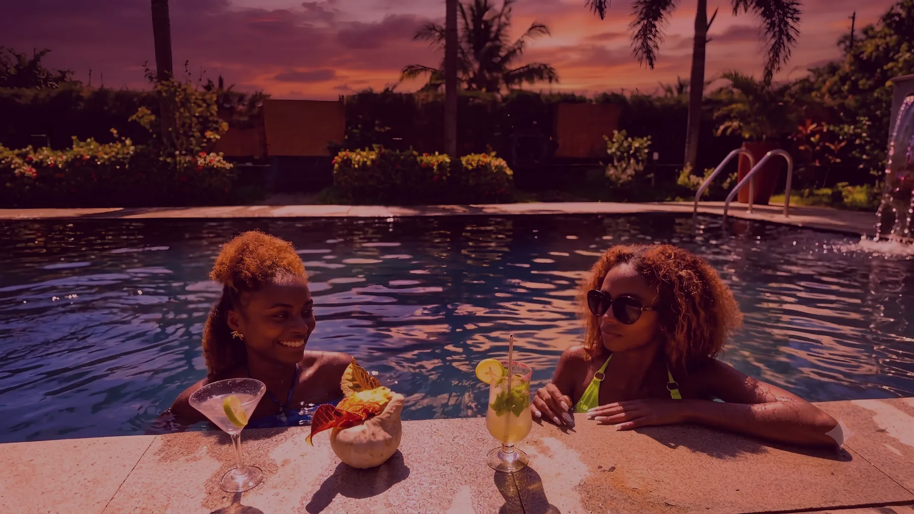 Representative hotel space: Two people relax by a swimming pool at sunset with drinks.