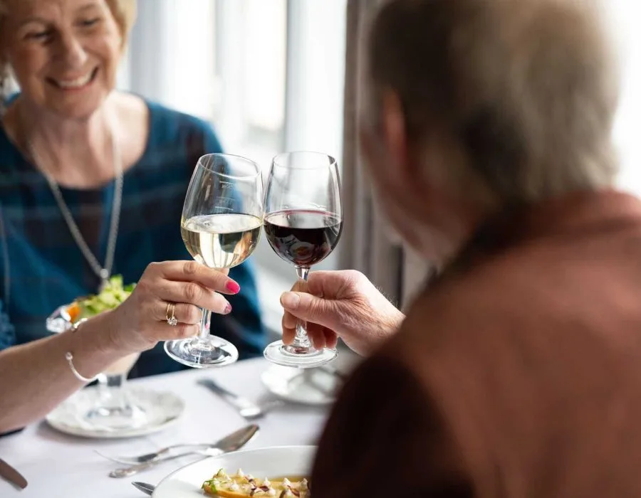 Espacio representativo del hotel: Dos personas alzan copas de vino mientras comen en una mesa.
