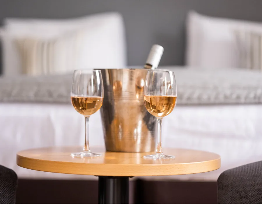 Espacio representativo del hotel: Una mesa redonda con dos copas y una botella frente a una cama.