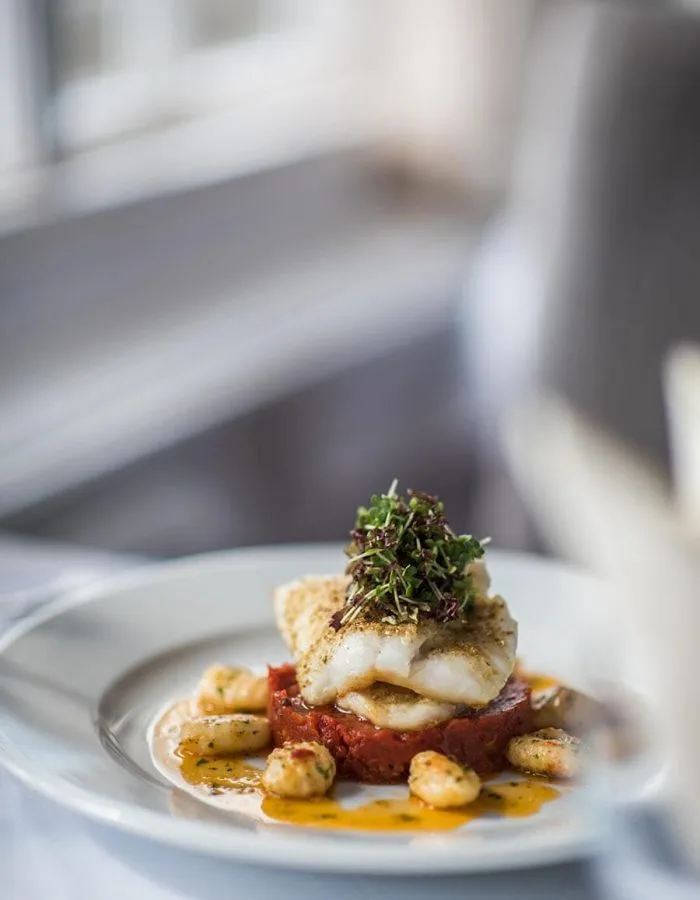 Espacio representativo del hotel: Un plato de pescado lleva hierbas por encima y se sirve sobre una salsa roja.