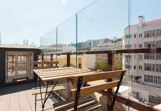 A rooftop terrace with wooden seating and glass railings overlooking nearby buildings.