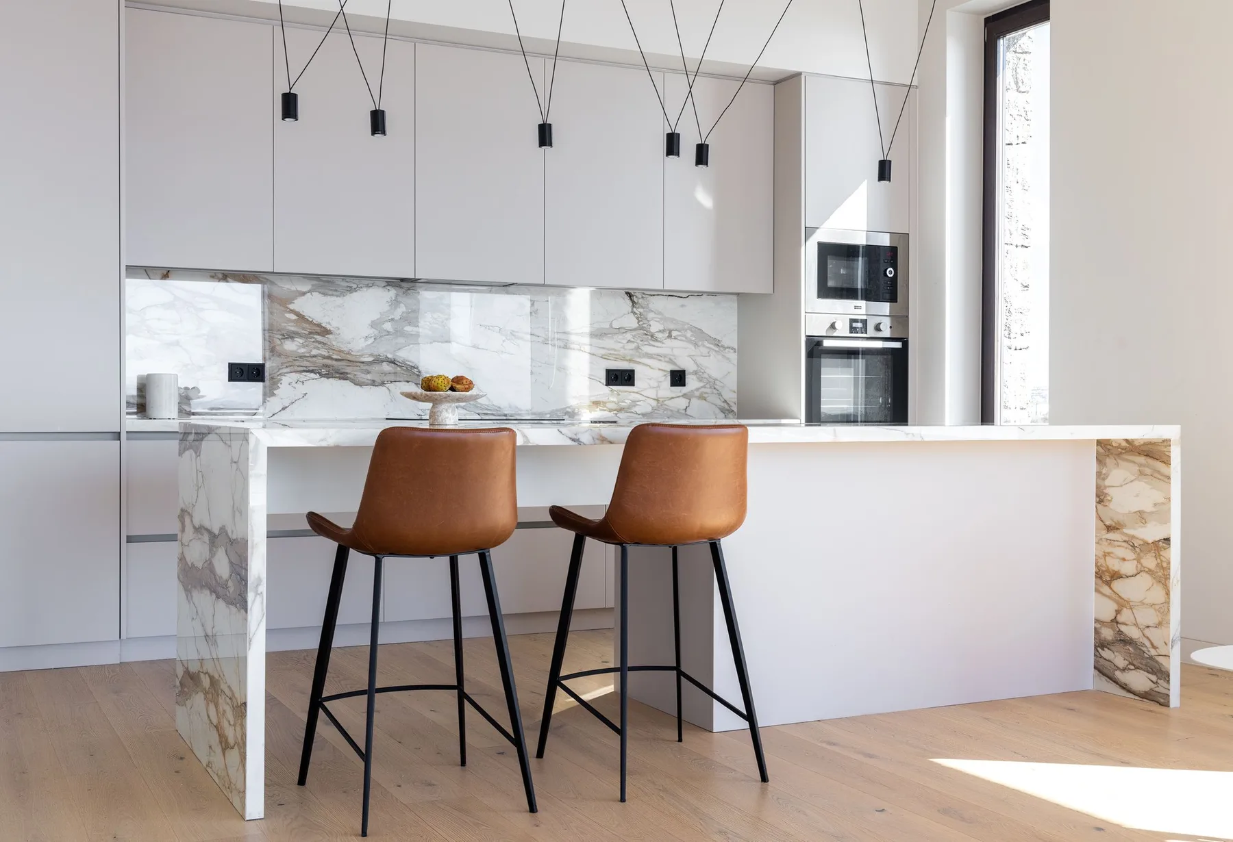 A modern kitchen with a large island, two stools, and pendant lights.