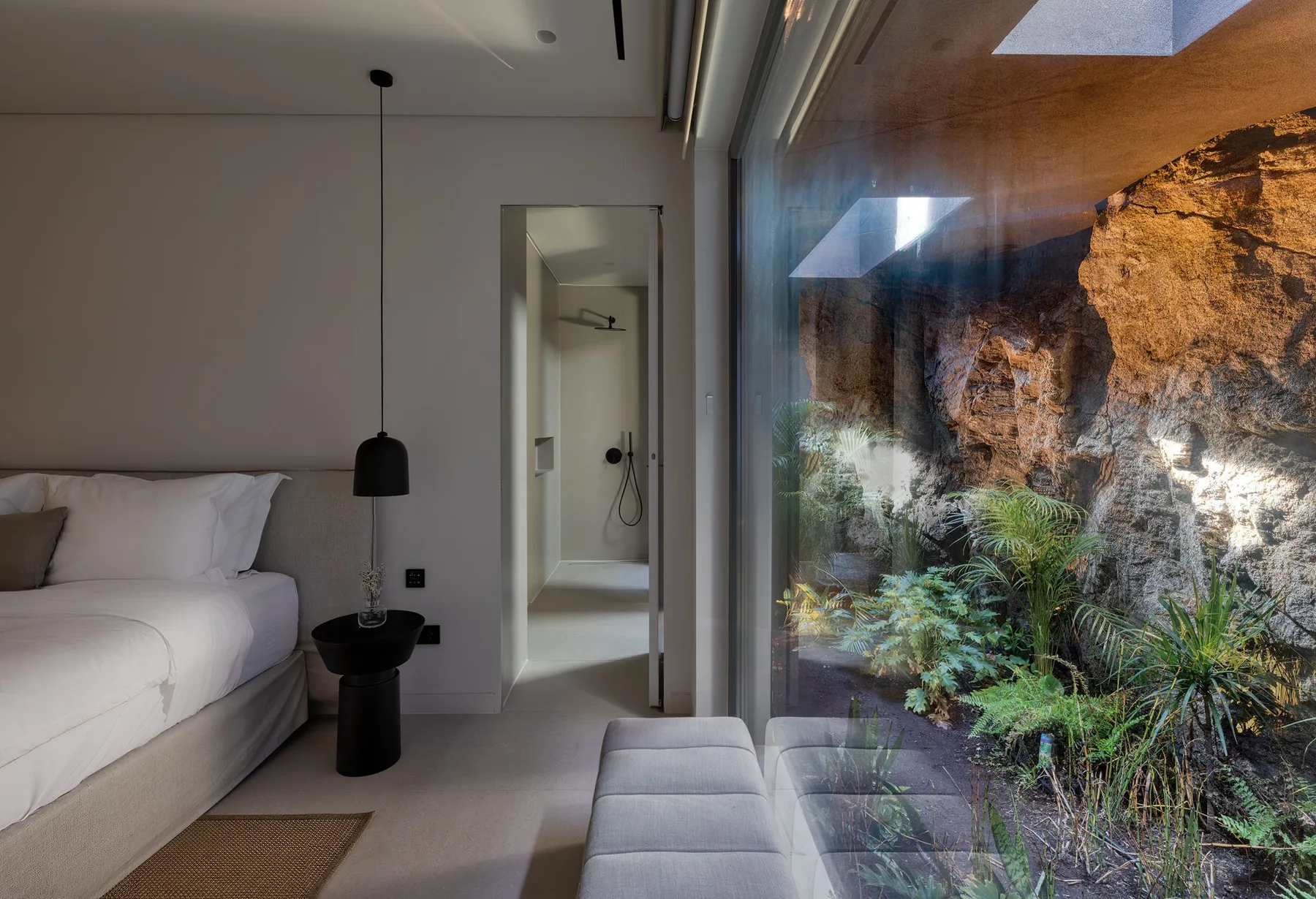 A bedroom with a bed beside a glass wall overlooking a rocky garden.