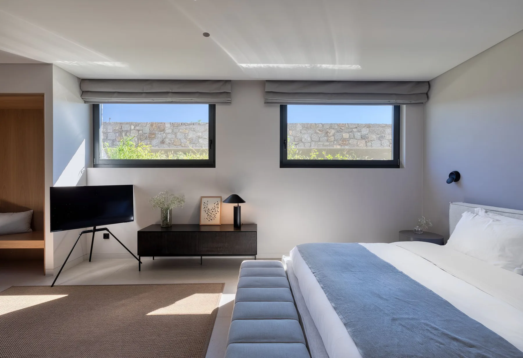 A bedroom with a bed, a television, and two windows.
