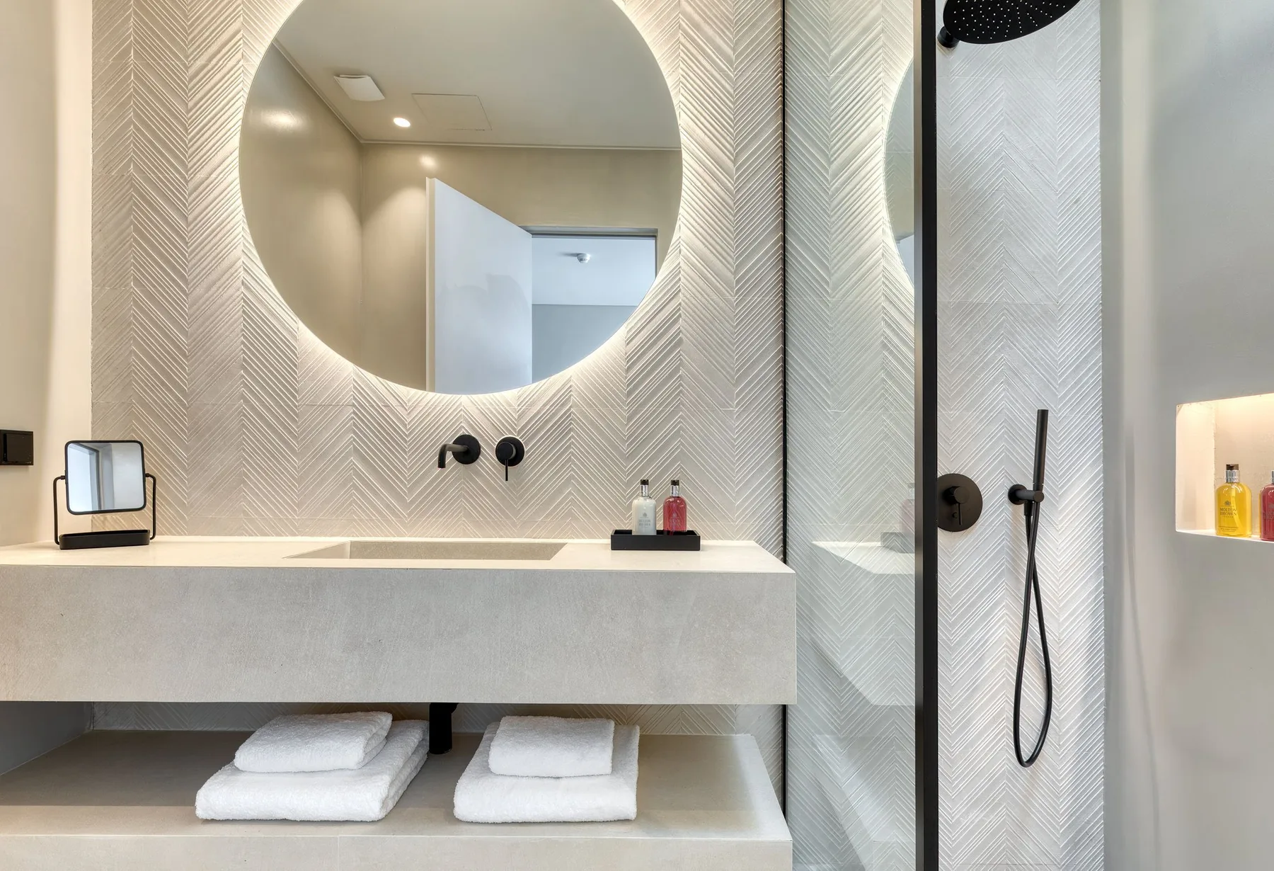 A modern bathroom with a round mirror above a wide sink and a glass shower.