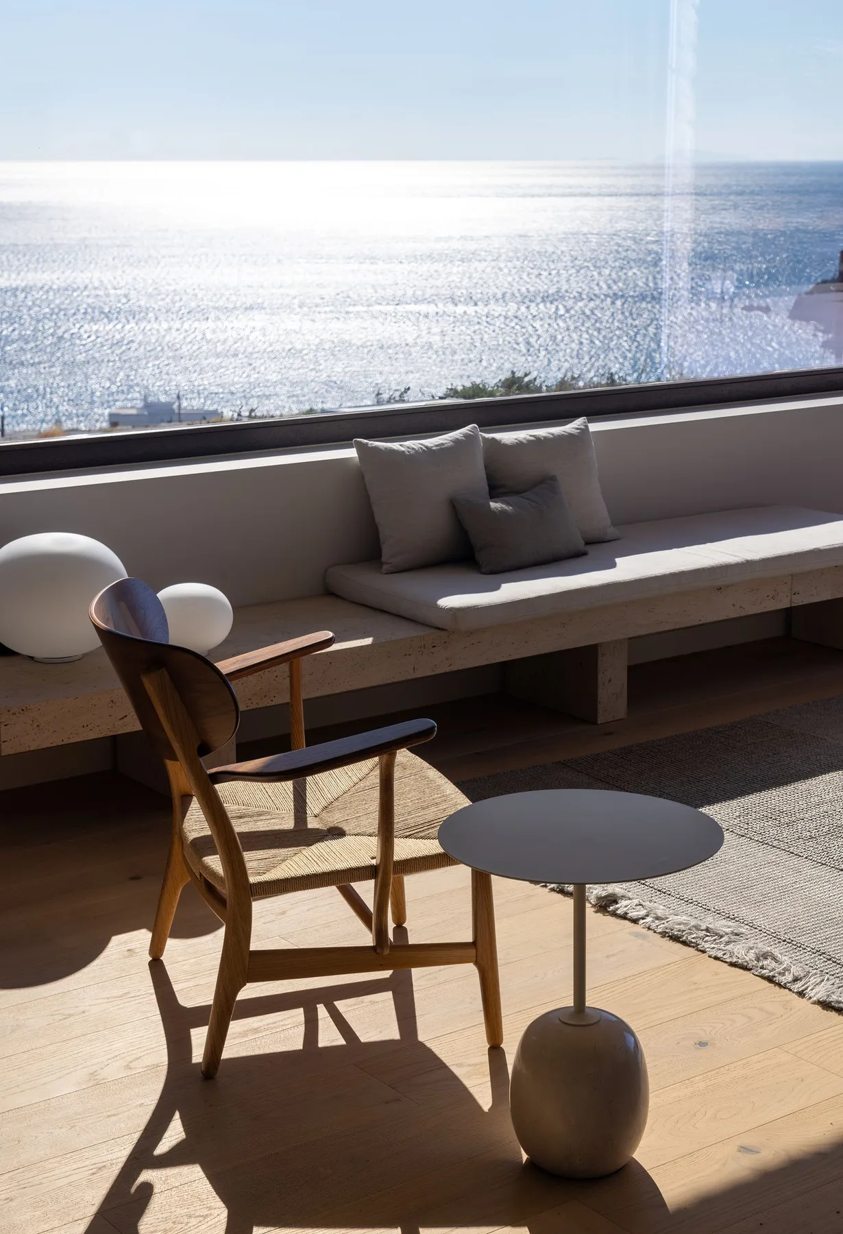 A seating area by a large window overlooks the sea, with cushions on a built-in bench.