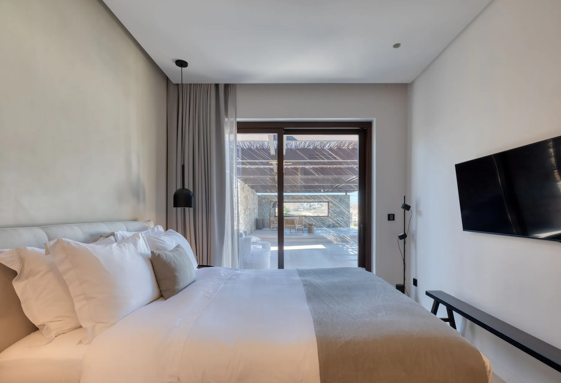 A bedroom with a bed facing sliding glass doors and a wall-mounted television.