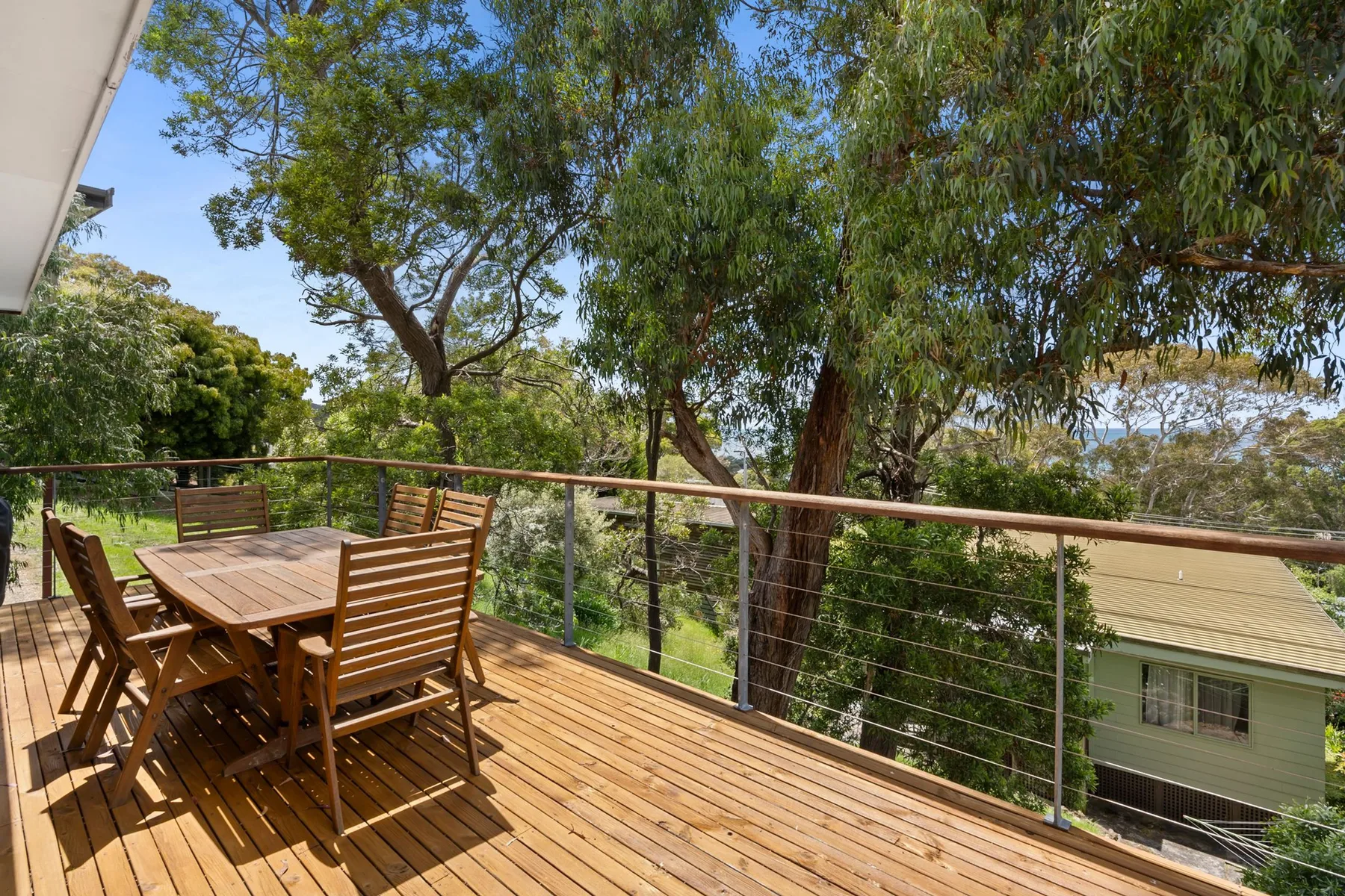 Una terraza de madera con asientos al aire libre da a árboles frondosos y una casa vecina.