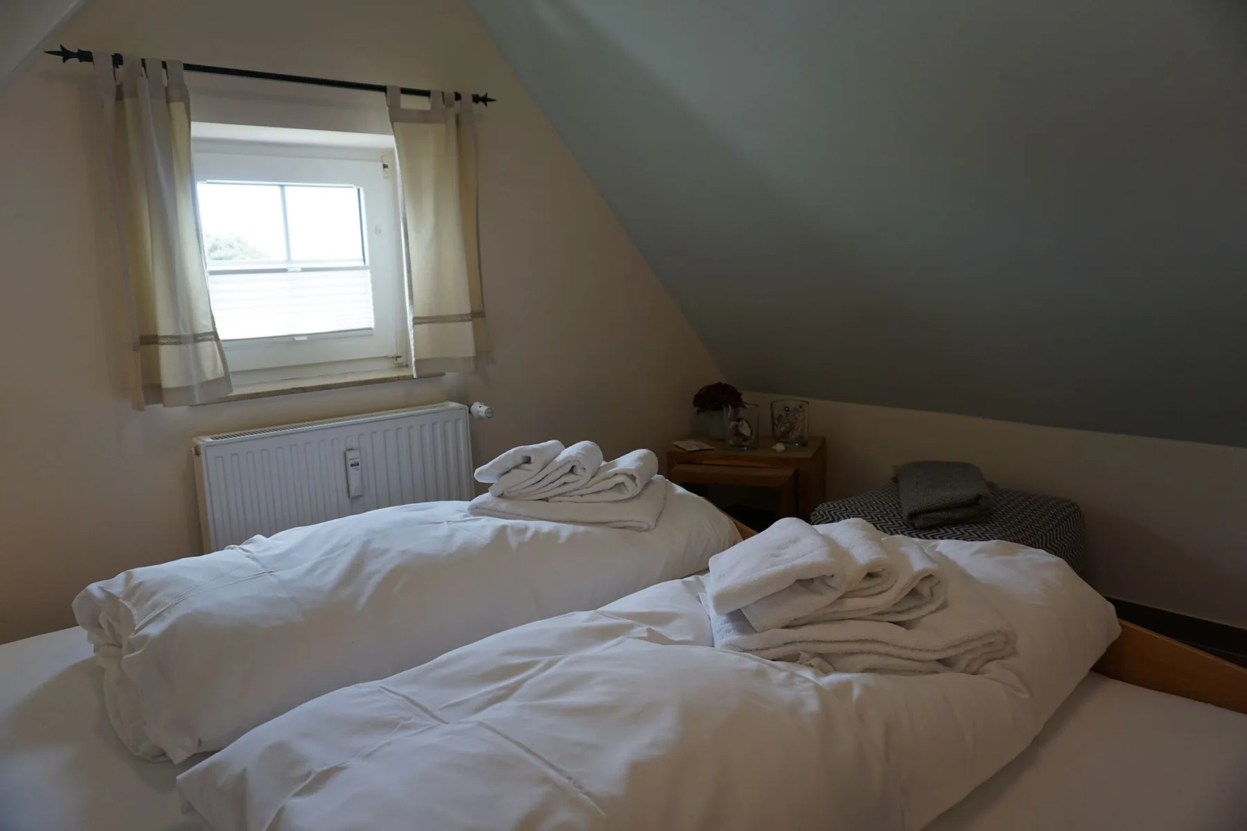 A bedroom with two beds beneath a sloped ceiling and a window.