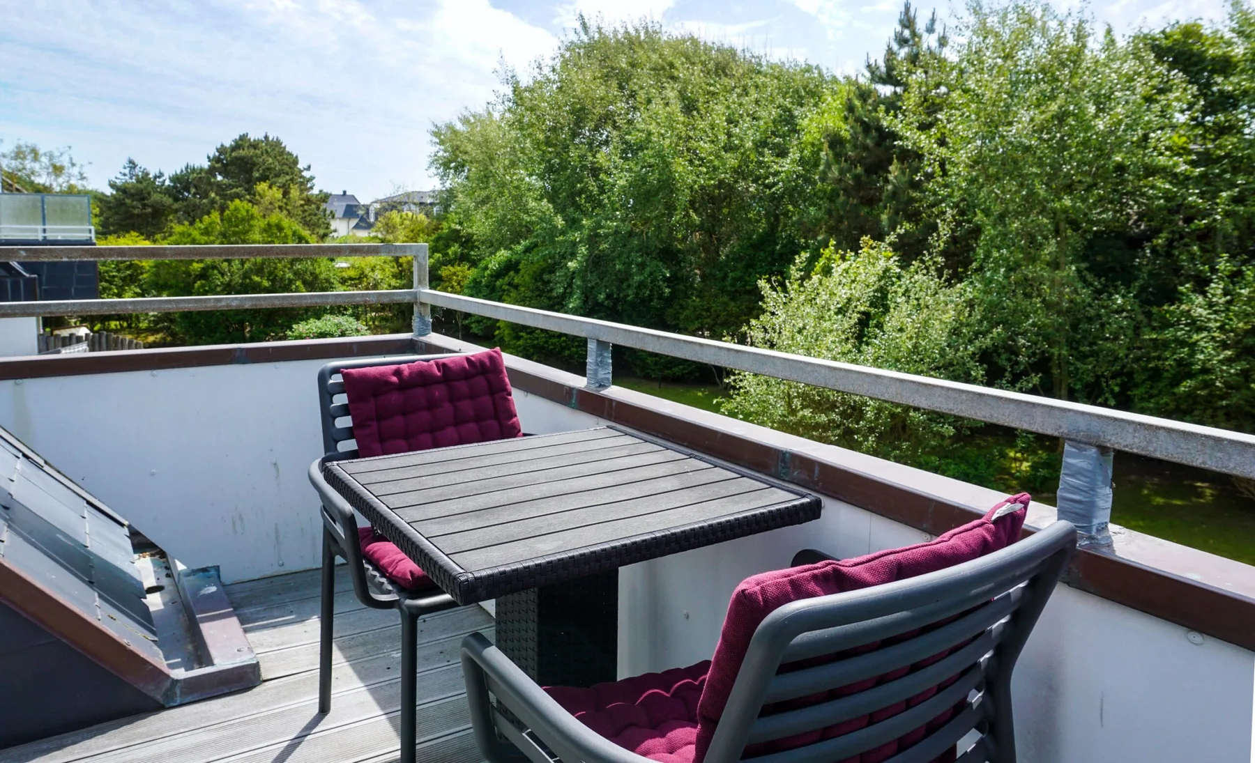 A balcony seating area with a table overlooks leafy trees.