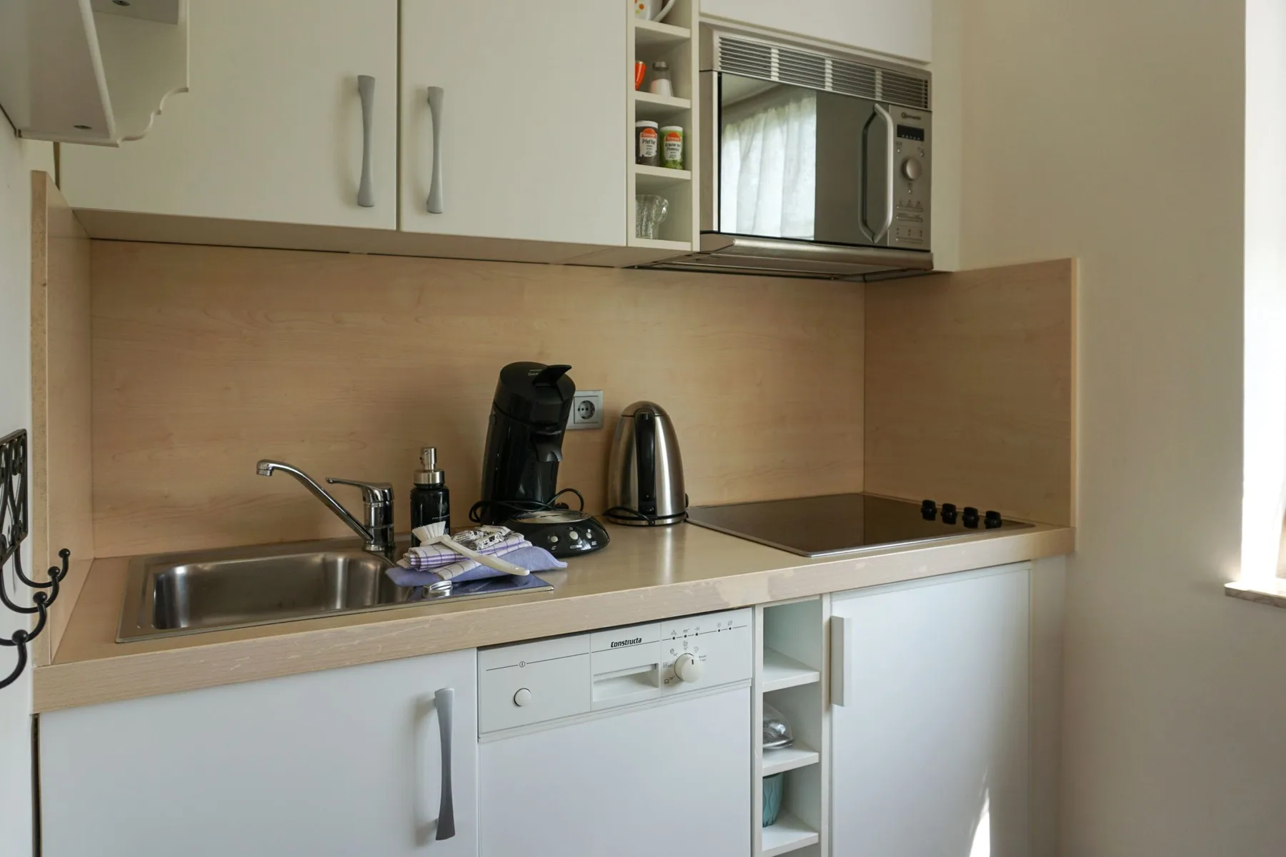 A compact kitchen with a sink, countertop appliances, and white cabinets.
