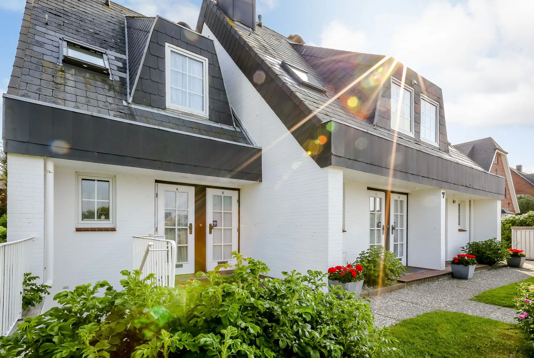 Shared amenity: A row of white cottages with dark roof windows borders a garden path.