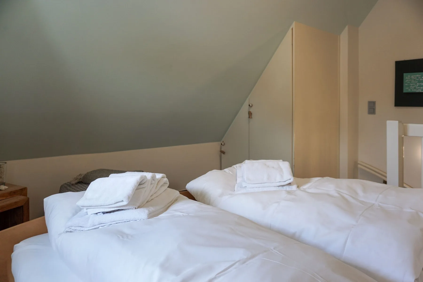A bedroom with beds dressed in white linens beneath a sloped ceiling.